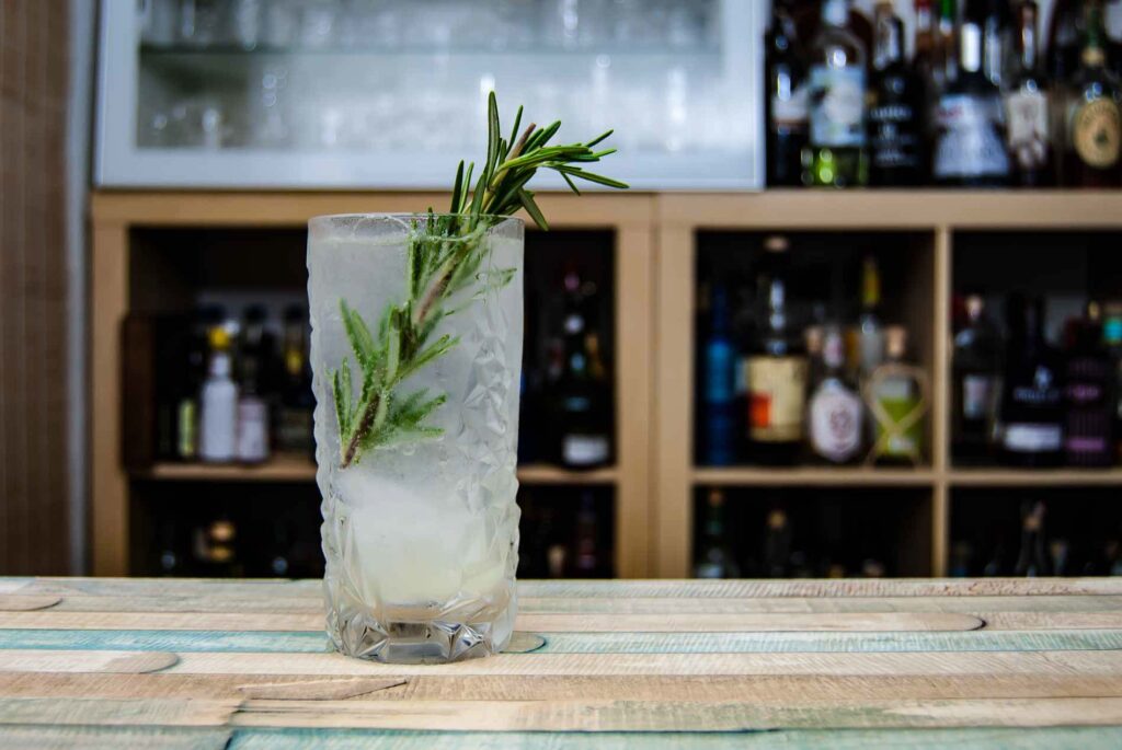 Ein mediterraner Gin Fizz mit einem Rosmarinzweig und einem Sprühstoß Olivenöl als Deko.